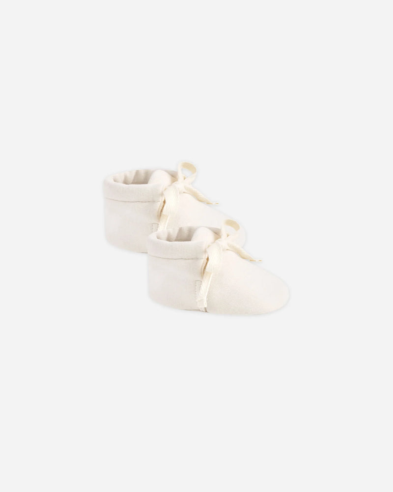Soft 100% organic cotton baby booties with adjustable ankle ties in natural beige, designed to keep infants’ feet snug and secure. Hypoallergenic and breathable for delicate newborn skin.